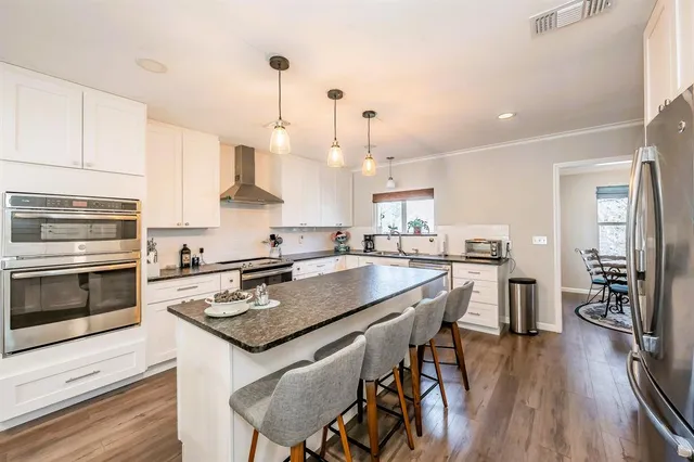 a kitchen with stainless steel appliances granite countertop a stove a sink dishwasher a refrigerator and a dining table with wooden floor