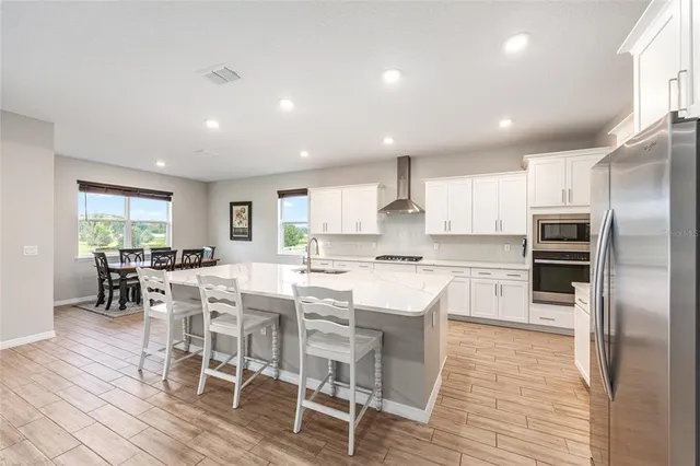 a kitchen with stainless steel appliances kitchen island granite countertop a refrigerator a stove a dining table and chairs