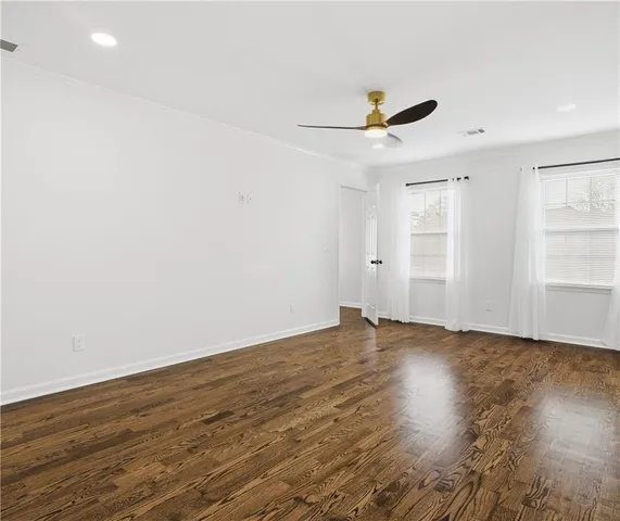 an empty room with wooden floor ceiling fan and windows