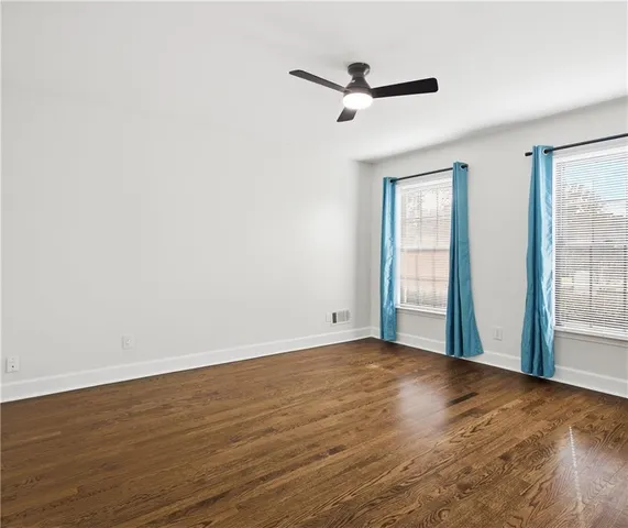 an empty room with wooden floor fan and windows