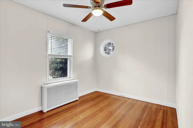 an empty room with wooden floor chandelier fan and windows