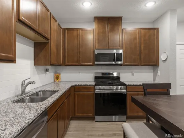 a kitchen with granite countertop a table chairs microwave and refrigerator