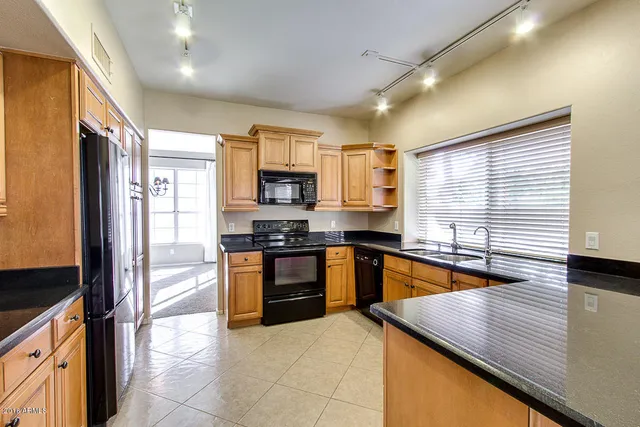 a kitchen with stainless steel appliances granite countertop a refrigerator a sink dishwasher a stove top oven and a dining table with wooden floor