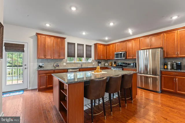 a kitchen with stainless steel appliances granite countertop wooden cabinets a refrigerator a stove a sink and chairs