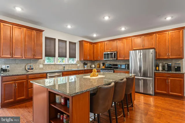 a kitchen with stainless steel appliances granite countertop a stove top oven a refrigerator a sink dishwasher and wooden cabinets with wooden floor