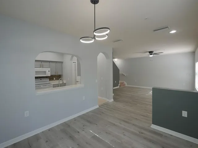 a view of an empty room with wooden floor and a ceiling fan