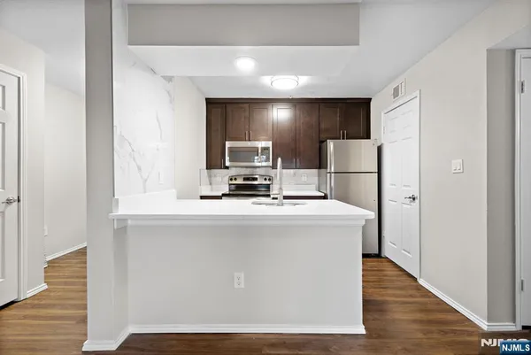 a view of kitchen with stainless steel appliances wooden floor dining table and chairs