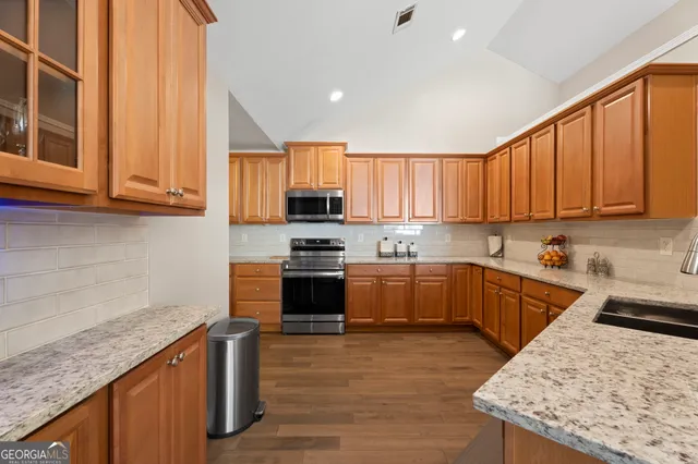 a kitchen with stainless steel appliances granite countertop a stove a sink dishwasher and a refrigerator with wooden cabinets