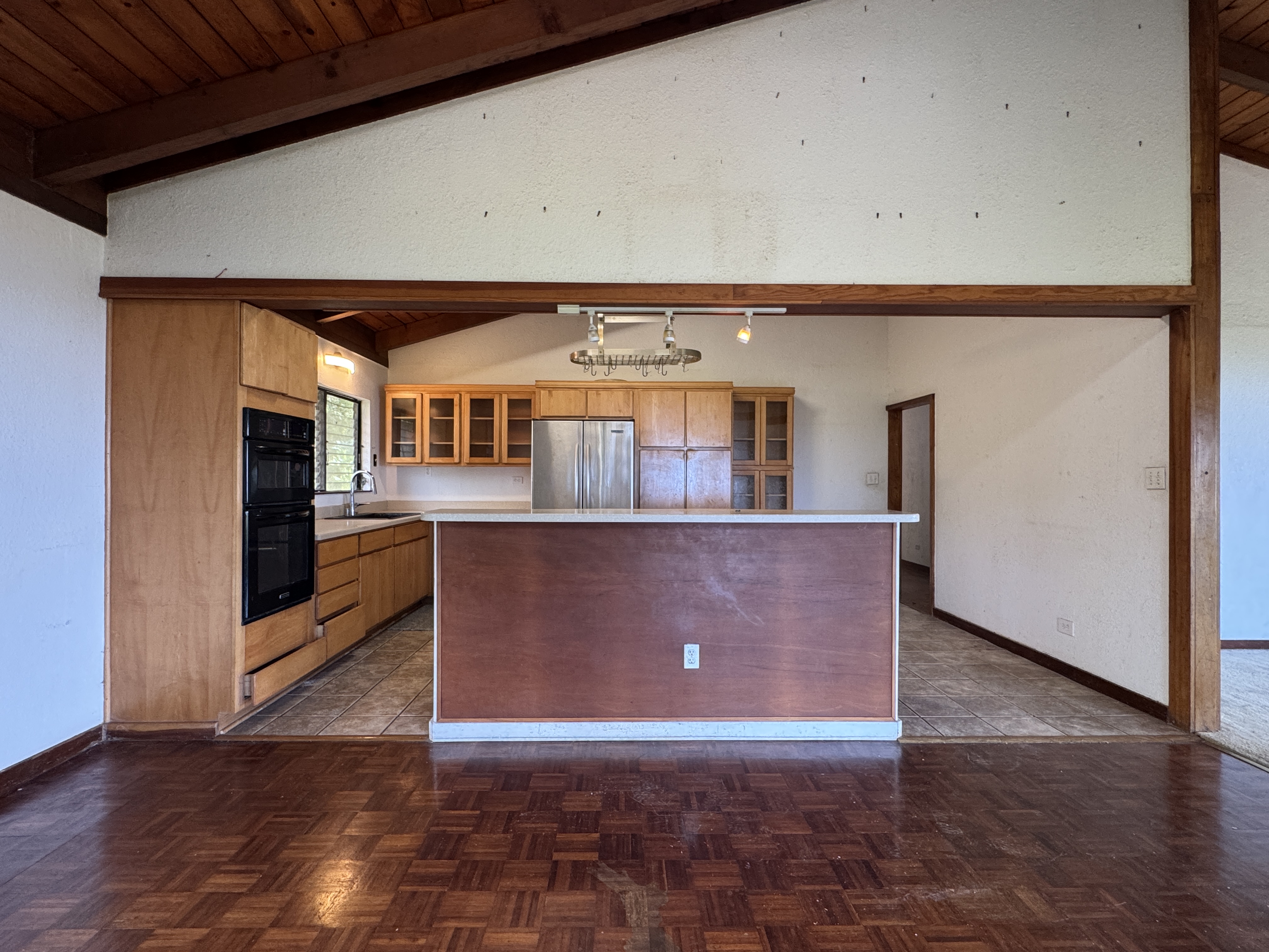84-5040 Hawaiʻi Belt Road Captain Cook, HI 96704 - Photo 10 of 30 an empty room with wooden floor and a kitchen