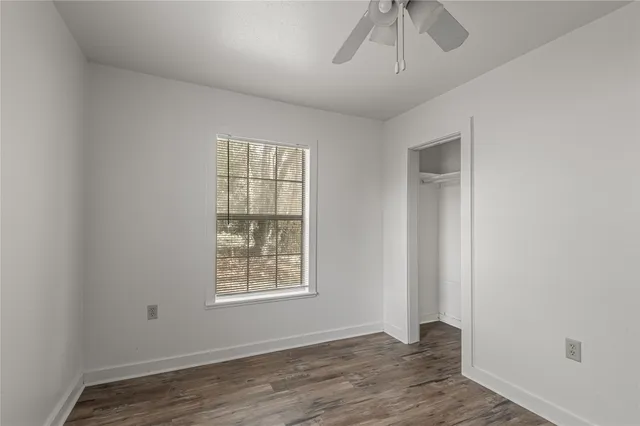 an empty room with wooden floor chandelier fan and windows