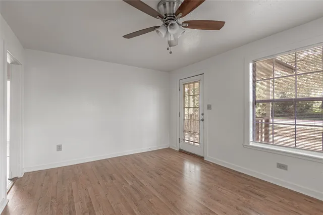 an empty room with wooden floor chandelier fan and windows
