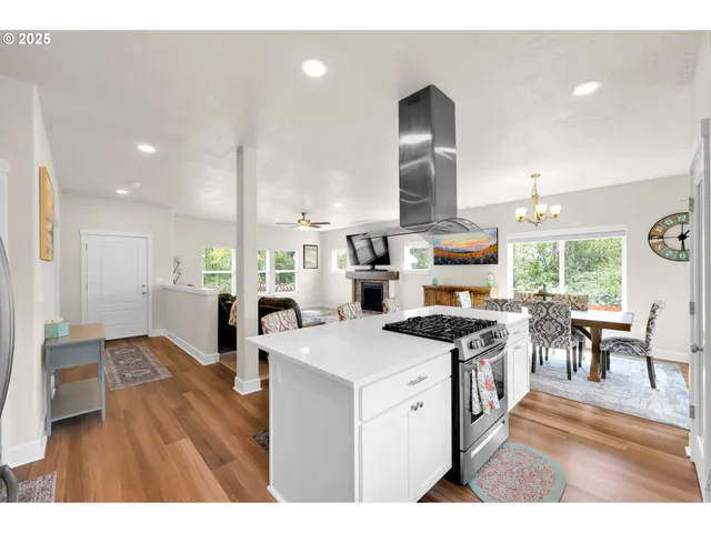 a open kitchen with stainless steel appliances kitchen island granite countertop a stove top oven a sink dishwasher and white cabinets with wooden floor