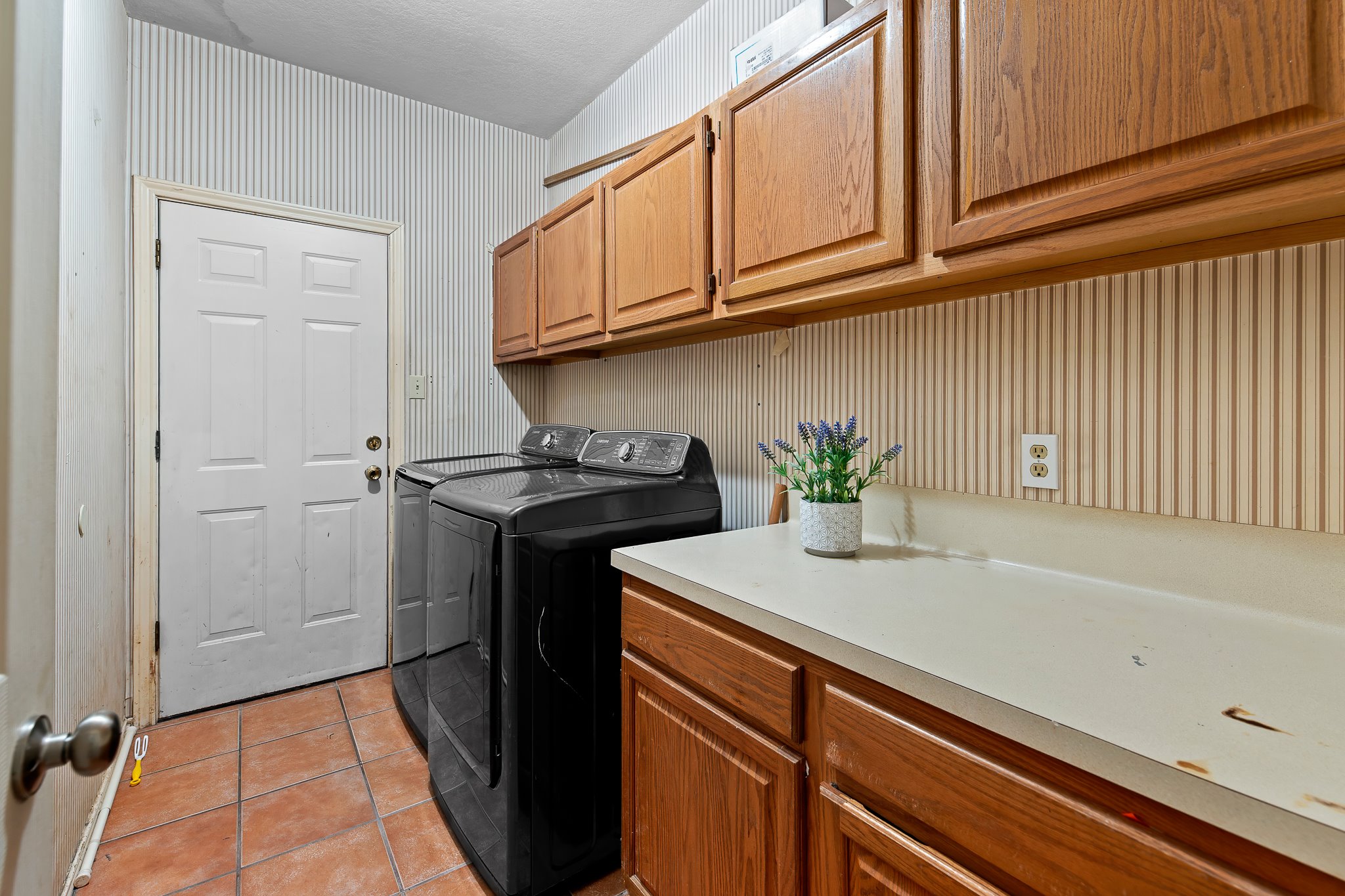 11737 Rydalwater Lane Austin, TX 78754 - Photo 22 of 40 Laundry area featuring terracotta-style floor tiling, a white paneled door, and wood cabinetry