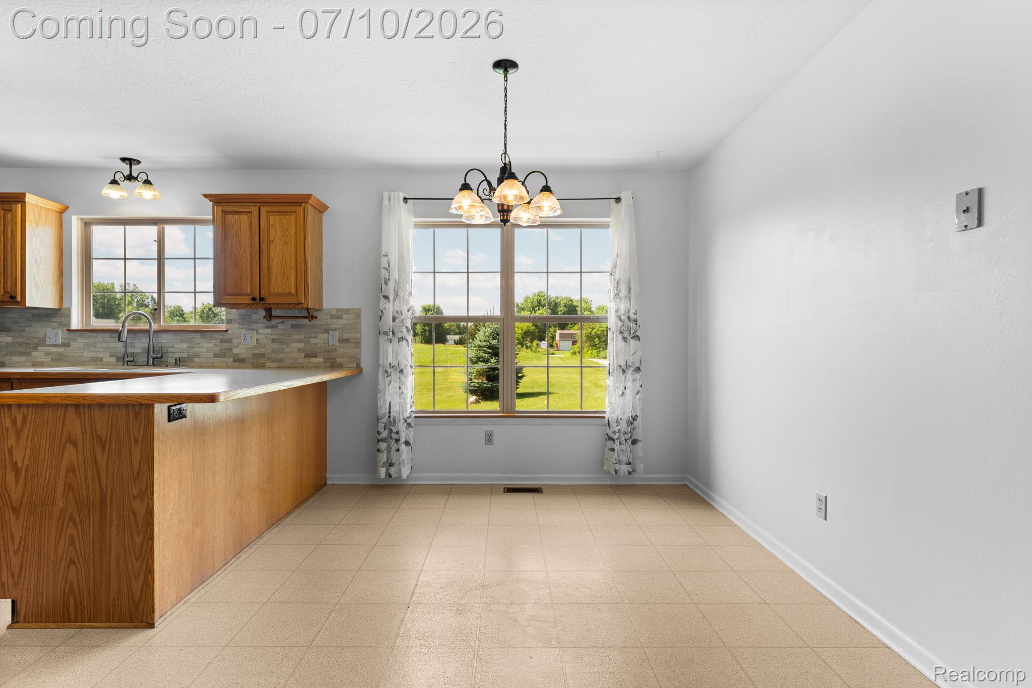 3144 North Nicholson Road Fowlerville, MI 48836 - Photo 37 of 70 Kitchen and dining area featuring light wood-finish cabinetry, a stone-look tile backsplash, a stainless steel faucet, and tile flooring