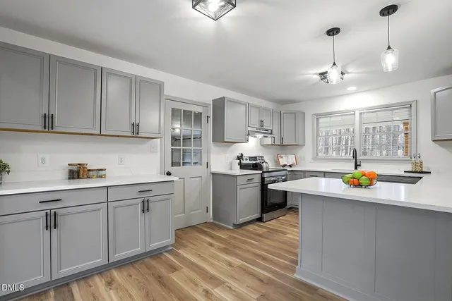 a kitchen with stainless steel appliances granite countertop a sink dishwasher a stove and white cabinets with wooden floor