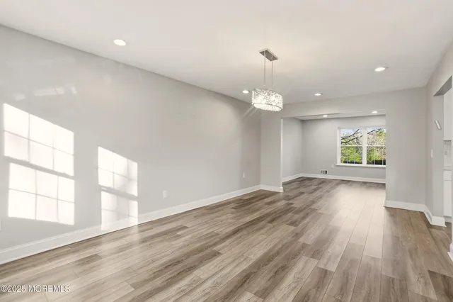 an empty room with wooden floor chandelier and windows