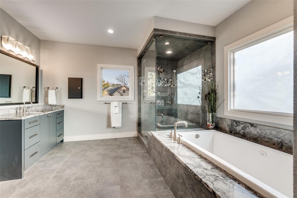 7912 Hanover Street Dallas, TX 75225 - Photo 7 of 29 Luxurious bathroom featuring a built-in soaking tub, a large walk-in glass shower with stone tile, a double vanity with stone countertops, and gray tile flooring
