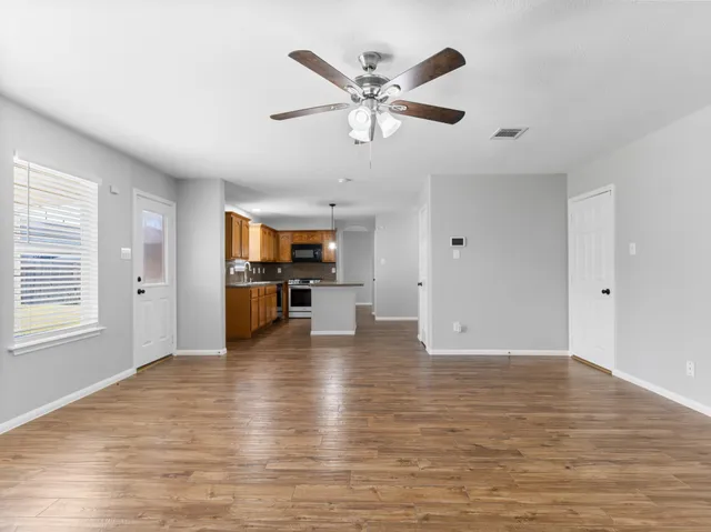 a view of an empty room with kitchen and window
