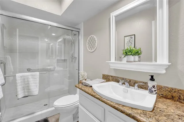 a bathroom with a granite countertop sink a toilet a mirror and shower
