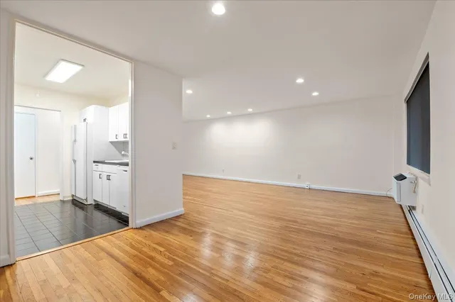 a view of an empty room with wooden floor and a kitchen