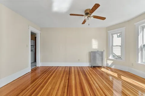 an empty room with wooden floor fan and windows