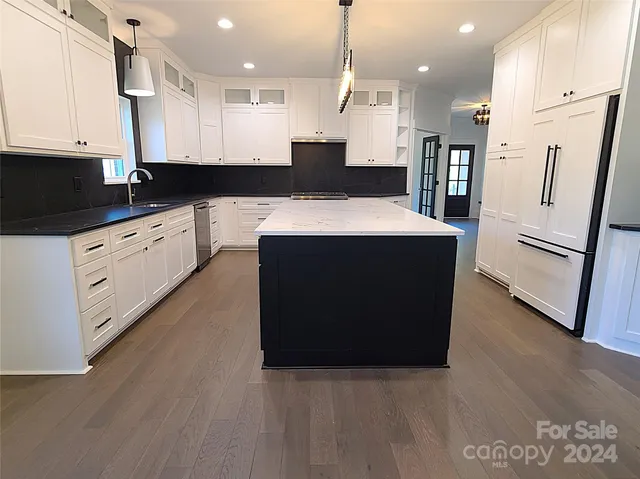 a large kitchen with stainless steel appliances granite countertop a refrigerator a oven a sink and white cabinets with wooden floor