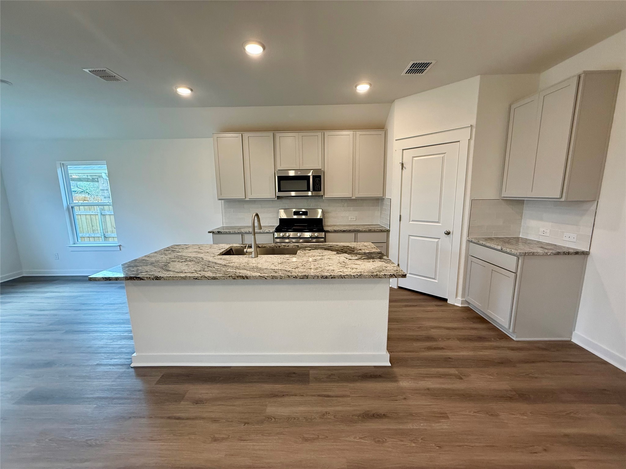 13605 Barn Chime Street Elgin, TX 78621 - Photo 3 of 20 a kitchen with kitchen island granite countertop wooden floors and white cabinets