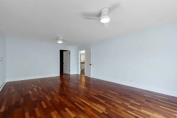 a view of an empty room with wooden floor and a ceiling fan
