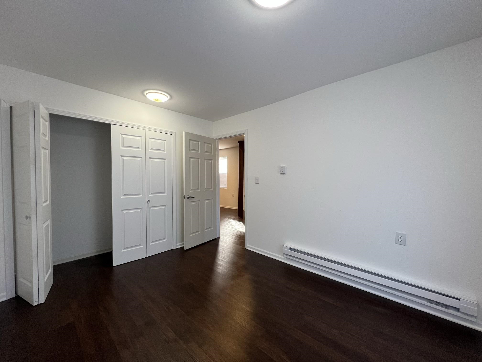 306 7th Street West Ashland, WI 54806 - Photo 10 of 25 Unfurnished bedroom featuring a baseboard radiator, dark wood-type flooring, and a closet