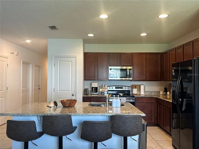 a kitchen with stainless steel appliances granite countertop a refrigerator a stove a sink a dining table and chairs