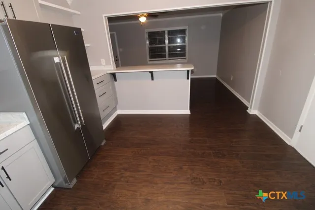 a view of a refrigerator in kitchen and an empty room with wooden floor