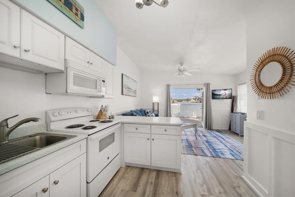 711 East Gulf Boulevard Indian Rocks Beach, FL 33785 - Photo 22 of 35 a kitchen with a sink dishwasher a stove and white cabinets with wooden floor
