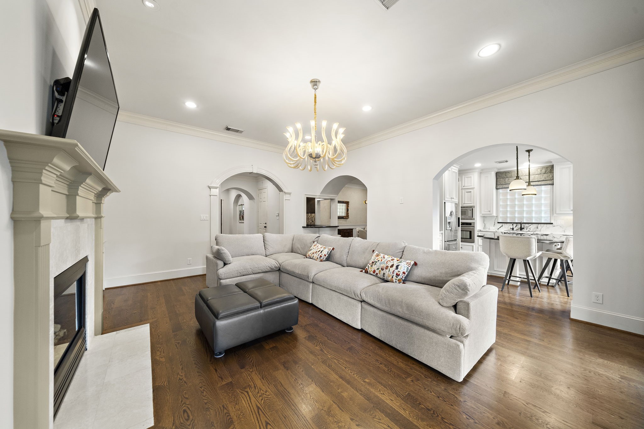 1229 Ripple Creek Drive Houston, TX 77057 - Photo 13 of 49 This inviting living room features hardwood floors, a cozy fireplace, and an elegant chandelier. It opens into a modern kitchen with white cabinetry and a breakfast bar, creating a seamless flow for entertaining.