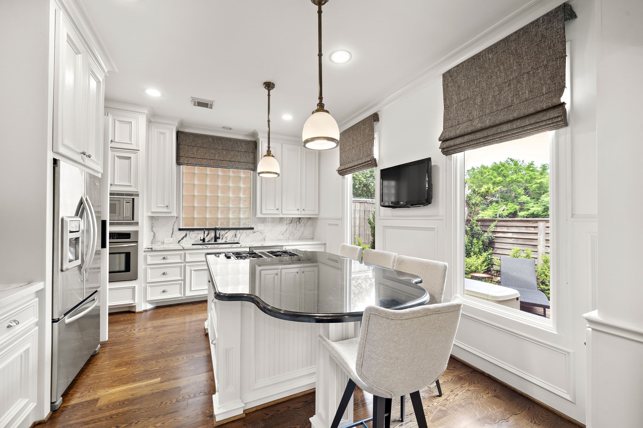 1229 Ripple Creek Drive Houston, TX 77057 - Photo 15 of 49 This kitchen features elegant white cabinetry, stainless steel appliances, and a sleek marble backsplash. It includes a central island with a breakfast bar, pendant lighting, and large windows offering a view of the outdoor space.