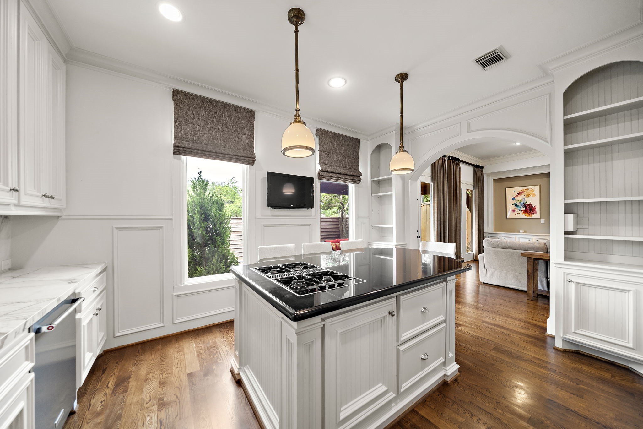 1229 Ripple Creek Drive Houston, TX 77057 - Photo 16 of 49 This kitchen features a spacious, open design with an island cooktop, elegant marble countertops, and hardwood floors. Ample natural light flows through large windows, and there's a seamless transition to the living area, highlighted by built-in shelving and classic pendant lighting.