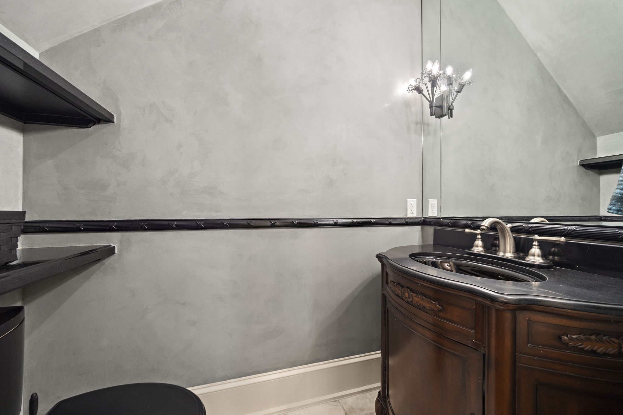 1229 Ripple Creek Drive Houston, TX 77057 - Photo 17 of 49 This bathroom features a stylish design with a dark wood vanity and an elegant black countertop. The walls have a smooth, modern finish, and there's a unique light fixture above the mirror, adding a touch of sophistication.