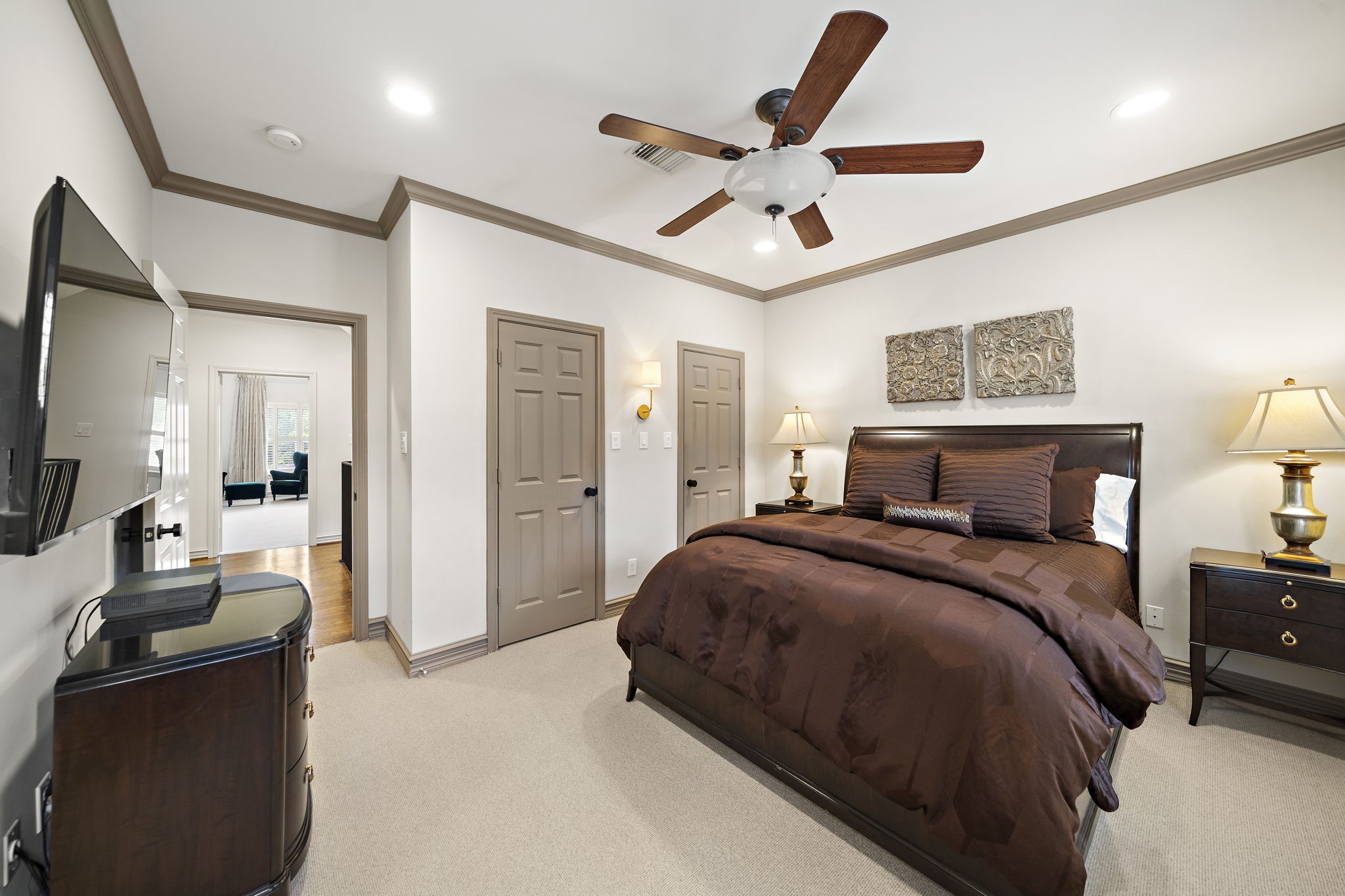1229 Ripple Creek Drive Houston, TX 77057 - Photo 18 of 49 This bedroom features a cozy ambiance with neutral walls and carpet, a dark wood bed set, and elegant decor. It has a ceiling fan, ample lighting, and a mounted TV, creating a comfortable and inviting space.
