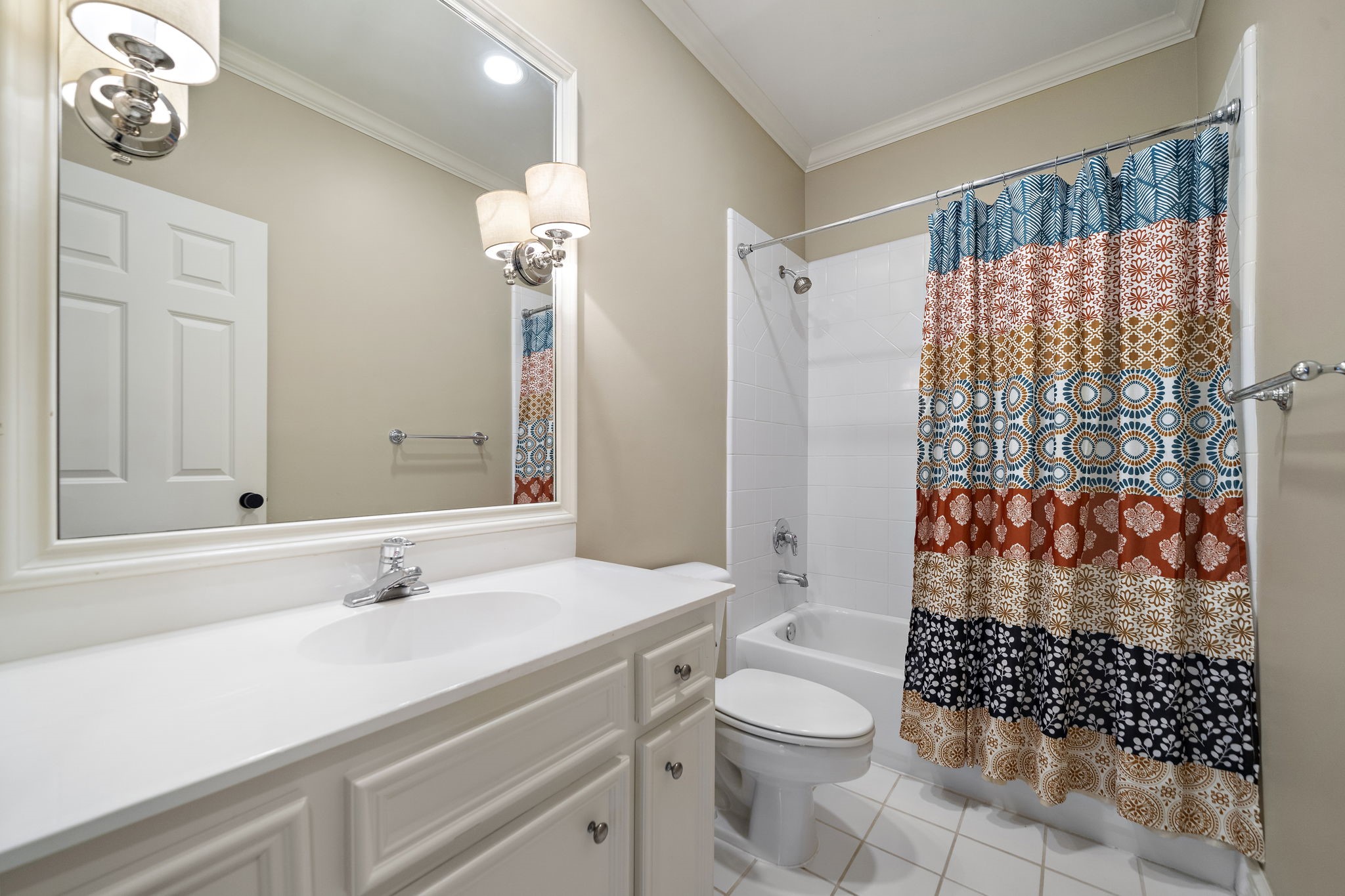 1229 Ripple Creek Drive Houston, TX 77057 - Photo 20 of 49 This bathroom features a clean, modern design with a white vanity, large mirror, and a colorful shower curtain. The space is well-lit with stylish wall-mounted lights and has a bathtub with a tiled surround.