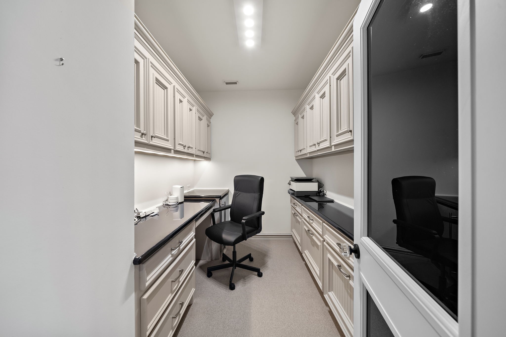 1229 Ripple Creek Drive Houston, TX 77057 - Photo 22 of 49 This photo shows a compact, well-organized home office or study with built-in cabinets, a black countertop, and a swivel chair. It's well-lit and designed for efficiency and storage.