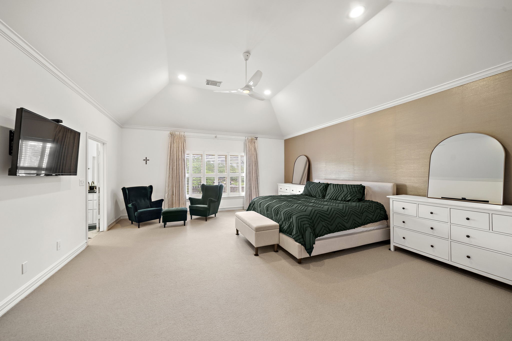 1229 Ripple Creek Drive Houston, TX 77057 - Photo 23 of 49 This spacious bedroom features high vaulted ceilings, a large window with elegant drapes, and ample natural light. It includes a cozy seating area, a wall-mounted TV, and a stylish bed with matching dressers. The room's neutral tones create a serene atmosphere, perfect for relaxation.
