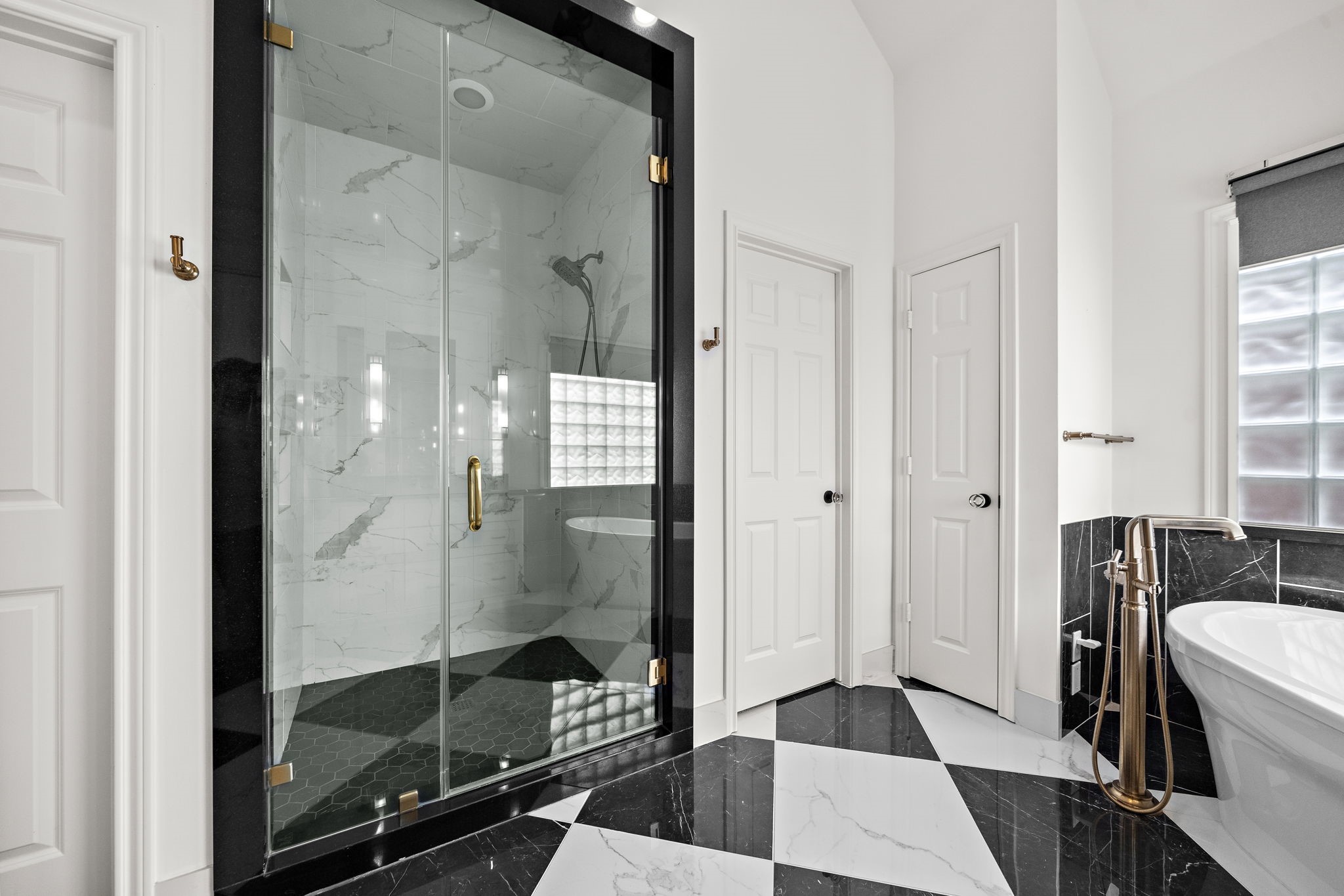 1229 Ripple Creek Drive Houston, TX 77057 - Photo 26 of 49 Modern bathroom with a luxurious feel, featuring a spacious glass-enclosed shower with elegant marble-style tiling. It has black and white checkered flooring, a freestanding bathtub, and sleek fixtures, creating a sophisticated atmosphere.