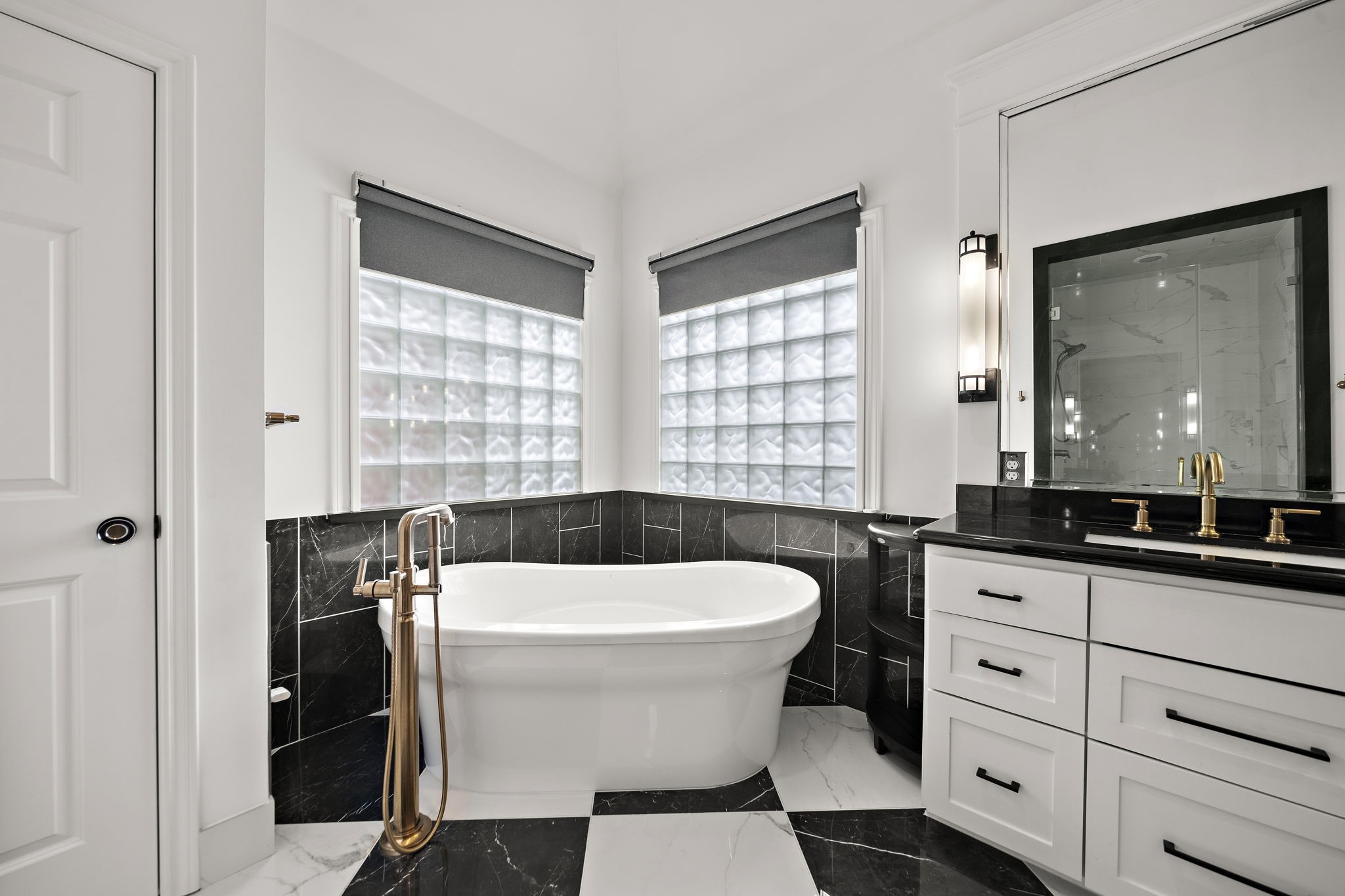 1229 Ripple Creek Drive Houston, TX 77057 - Photo 27 of 49 This modern bathroom features a sleek freestanding tub against black tile accents, a stylish vanity with gold fixtures, and ample natural light through frosted windows for privacy.