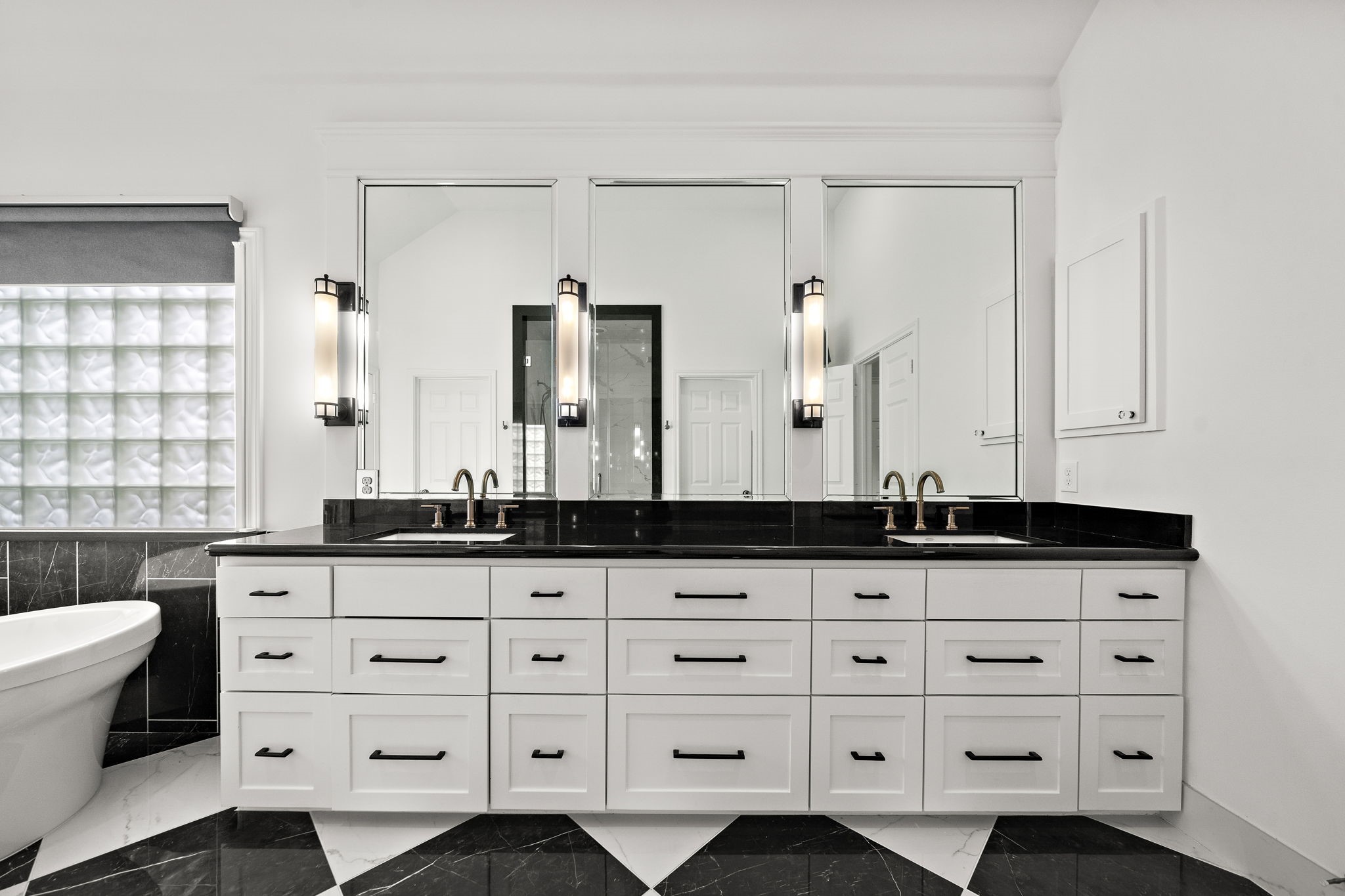 1229 Ripple Creek Drive Houston, TX 77057 - Photo 28 of 49 This bathroom features a sleek, modern design with a double vanity, black countertops, and ample storage. It includes elegant lighting fixtures, large mirrors, and a luxurious freestanding bathtub against a textured glass block window. The contrasting black and white tile adds a touch of sophistication.