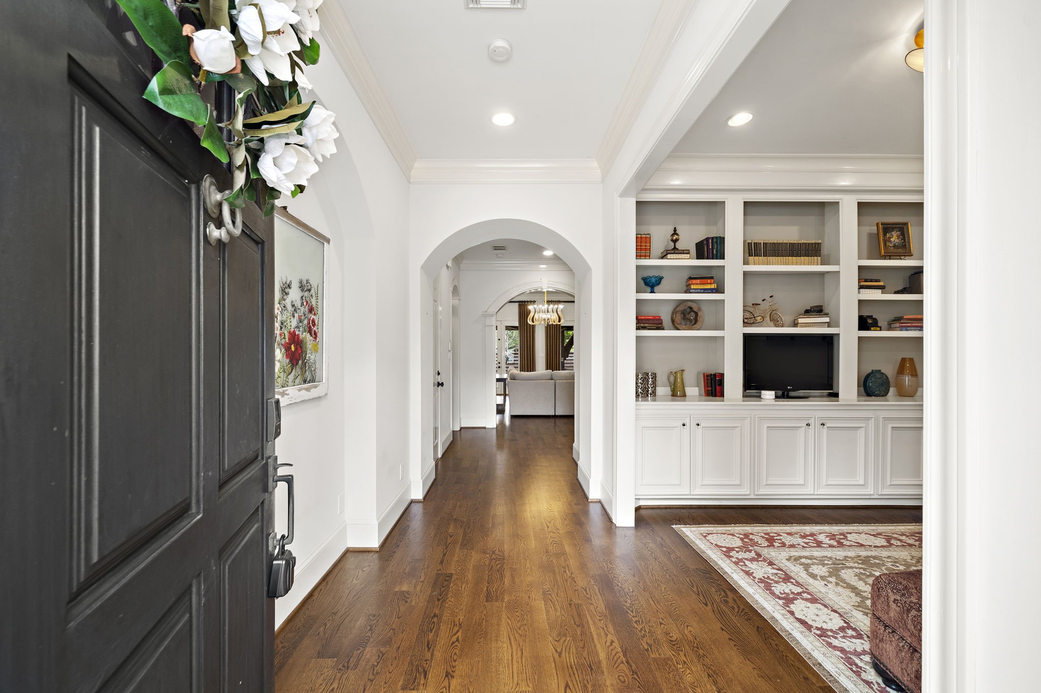 1229 Ripple Creek Drive Houston, TX 77057 - Photo 3 of 49 This photo showcases a welcoming entryway with hardwood floors, an elegant archway, and built-in shelving. The space is bright and inviting, leading to a living area with a view of a chandelier.