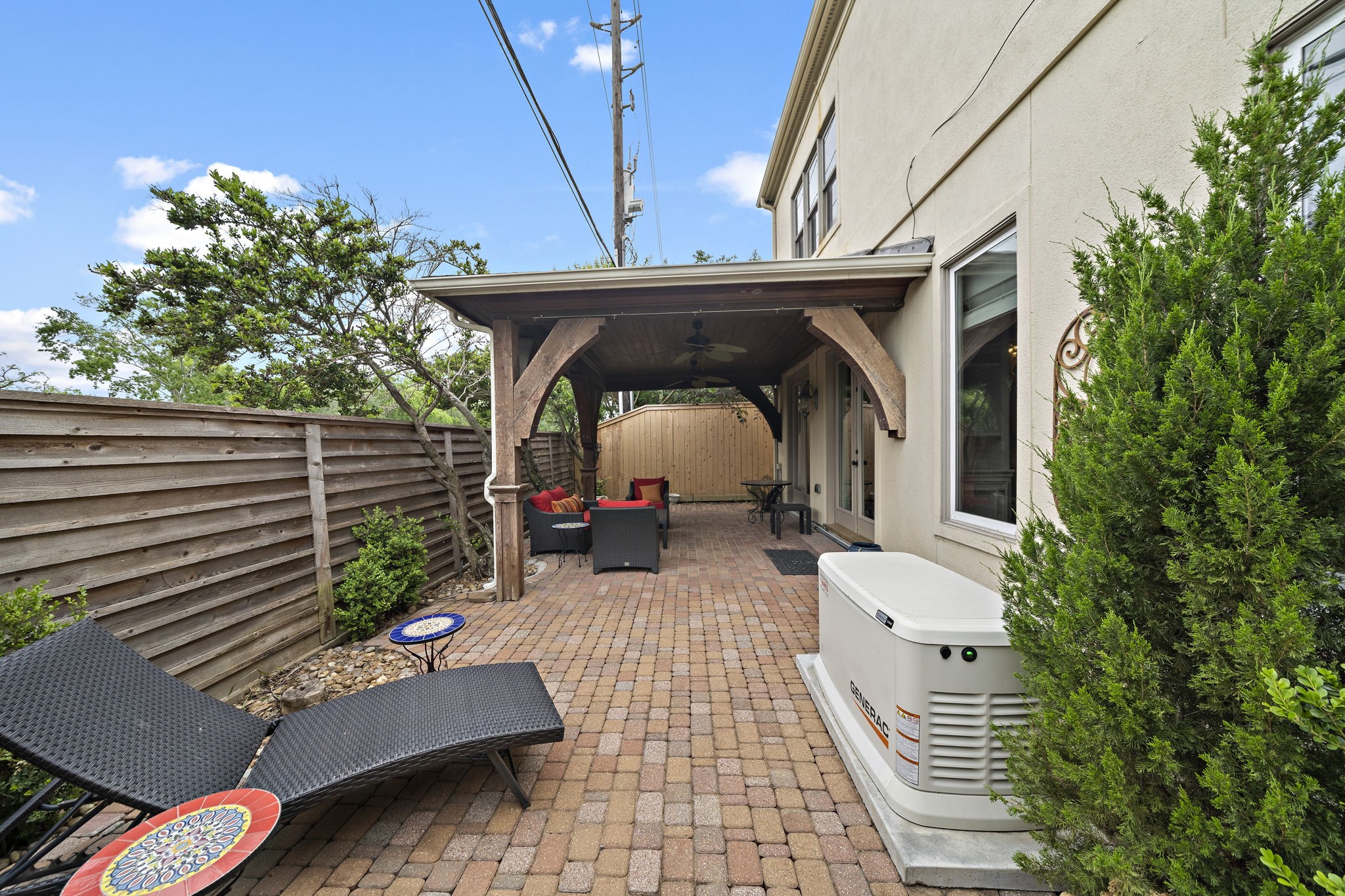 1229 Ripple Creek Drive Houston, TX 77057 - Photo 33 of 49 This photo showcases a cozy, covered patio with a wooden ceiling and ceiling fans, featuring brick flooring and comfortable outdoor seating. The space is surrounded by a privacy fence and landscaped with greenery, providing a serene outdoor retreat.