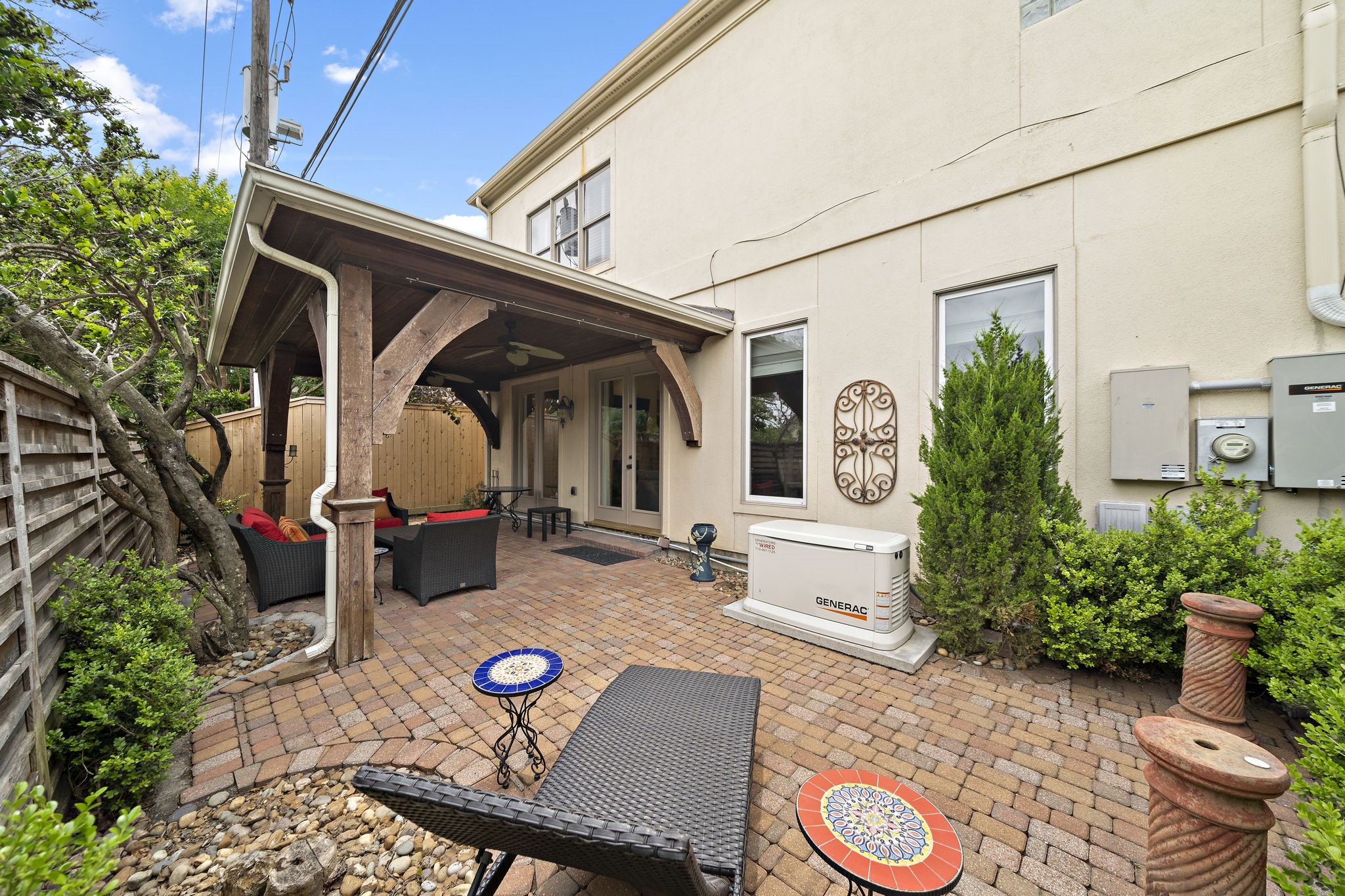 1229 Ripple Creek Drive Houston, TX 77057 - Photo 34 of 49 This photo showcases a cozy outdoor patio area with a covered seating space, brick pavers, and a wooden privacy fence. Ideal for relaxation, it features comfortable seating, a small table, and lush greenery for a pleasant ambiance.