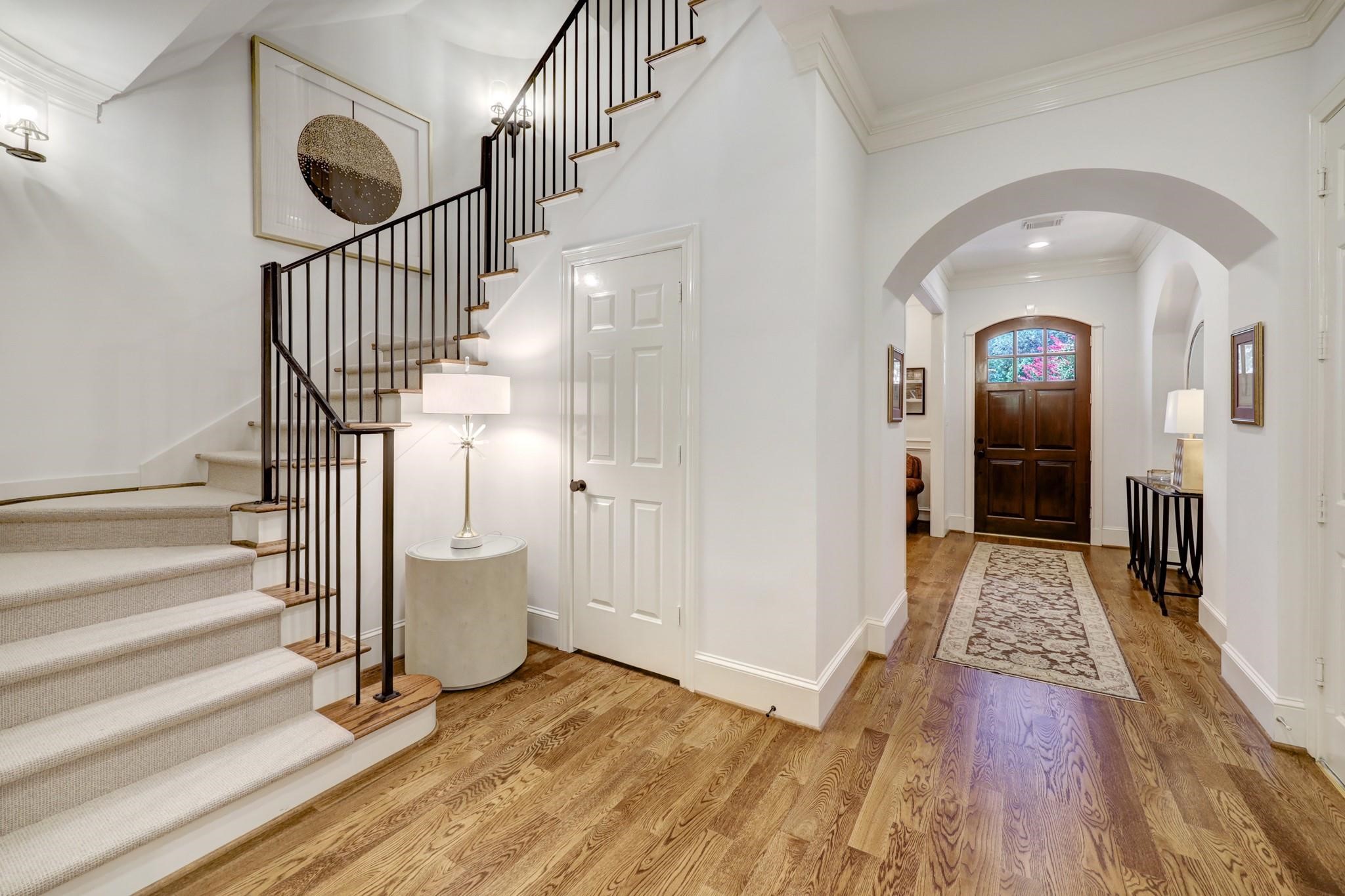 1229 Ripple Creek Drive Houston, TX 77057 - Photo 5 of 49 This photo showcases a welcoming foyer featuring hardwood floors and an elegant staircase with wrought iron railings. The space has high ceilings, arched doorways, and a wooden front door, creating a warm and inviting entrance.