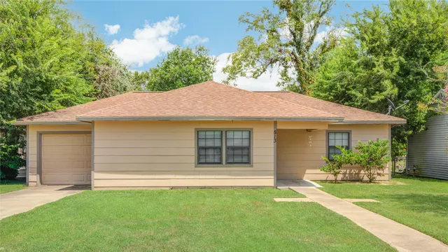 a view of a house with a yard plants and large tree