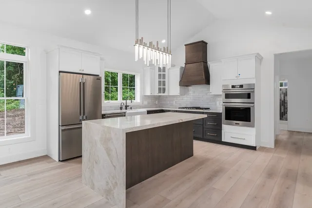 a kitchen with stainless steel appliances granite countertop a refrigerator a sink dishwasher a stove and a dining table with wooden floor