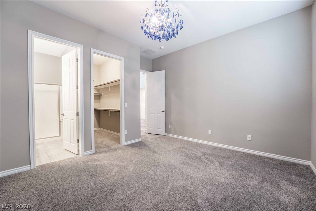 2787 Athens Ridge Drive Henderson, NV 89052 - Photo 11 of 31 A spacious bedroom featuring soft carpet and a striking chandelier, with an adjoining bathroom and walk-in closet.